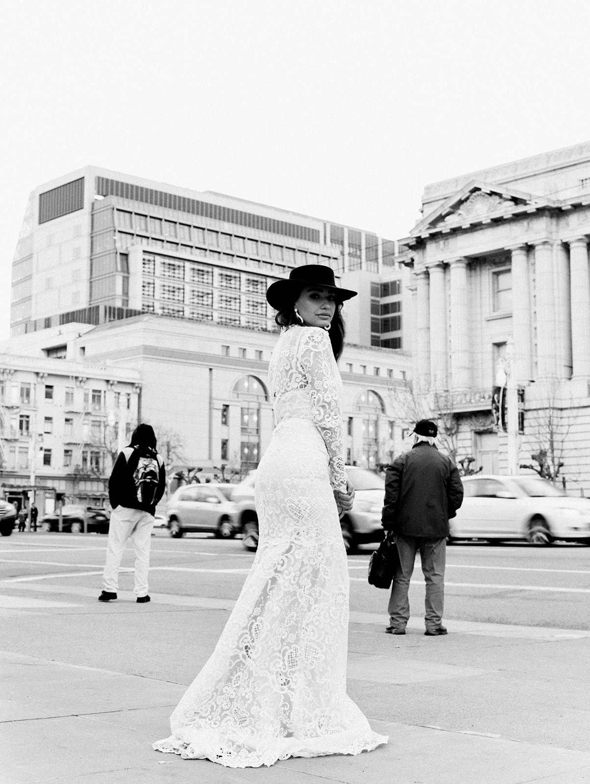 A female with long brunette hair posing for this San Francisco Bridal styled shoot in this black and white image. She wears a long sleeve lace fitted wedding gown. Her earrings are long and white. 
