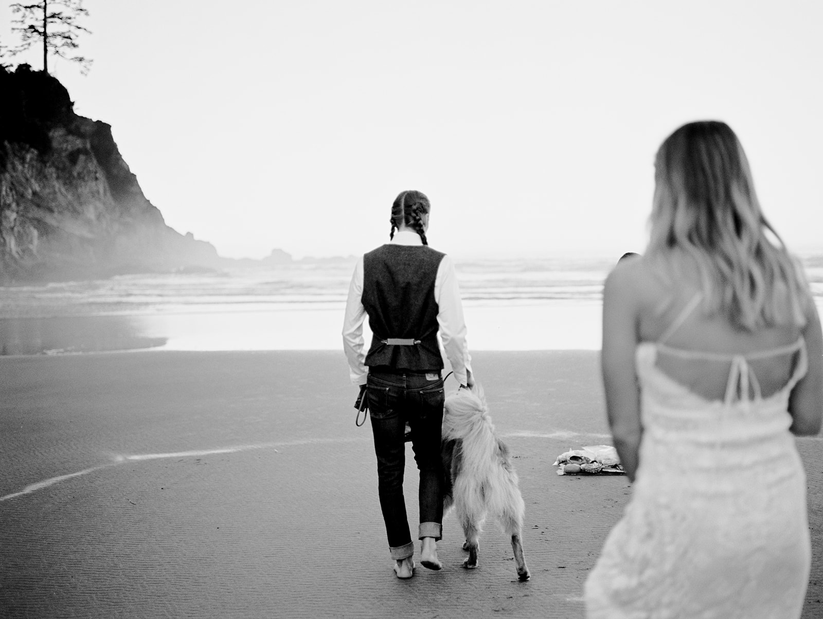 A black and white photo of the groom walking his dog and the bride following behind them, during their Oregon Coast Elopement.