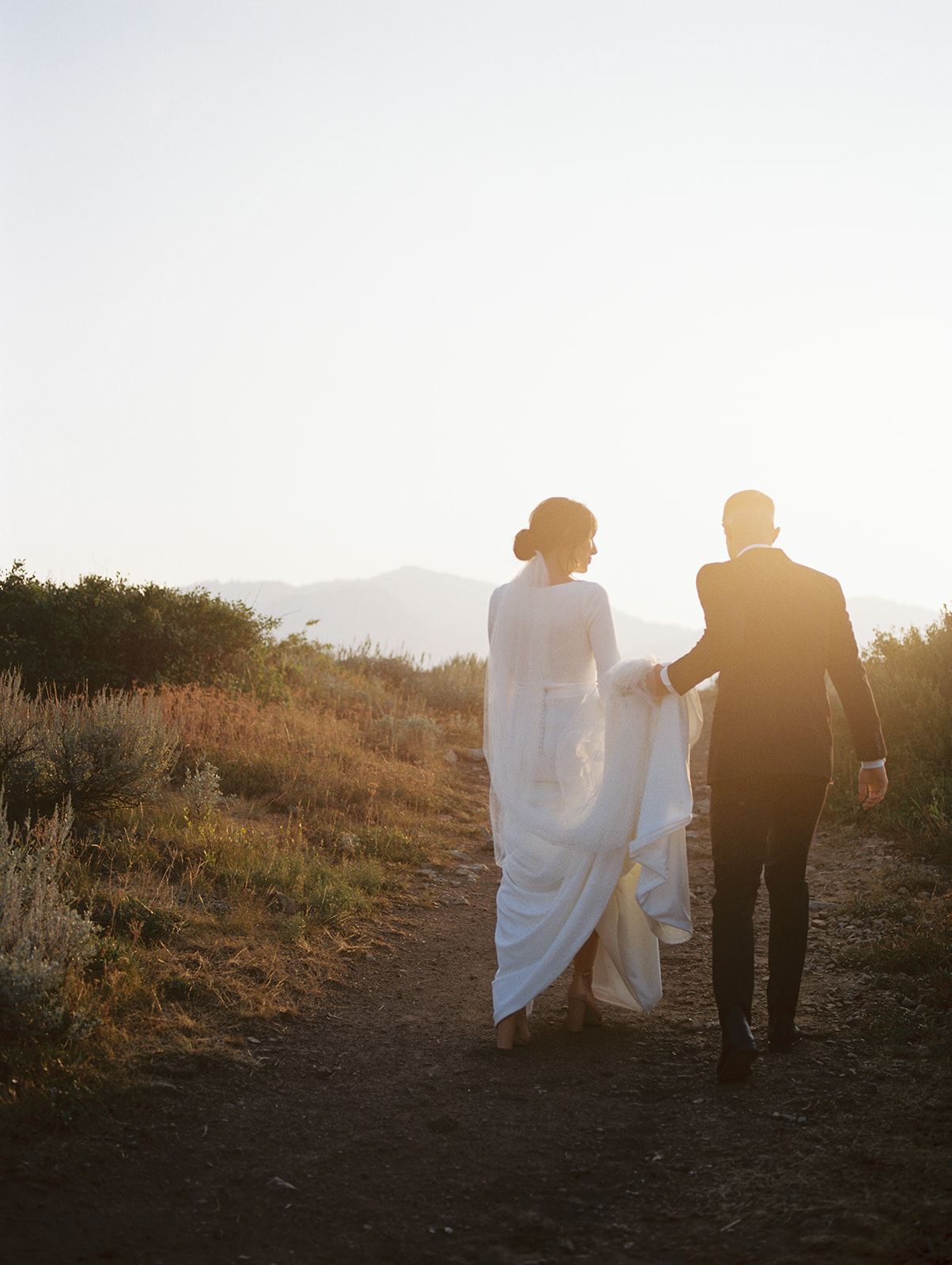 An image of couple portraits. Taken around sunset. The bride wears a white long sleeve fitted wedding gown. Where the groom wears a black suite.