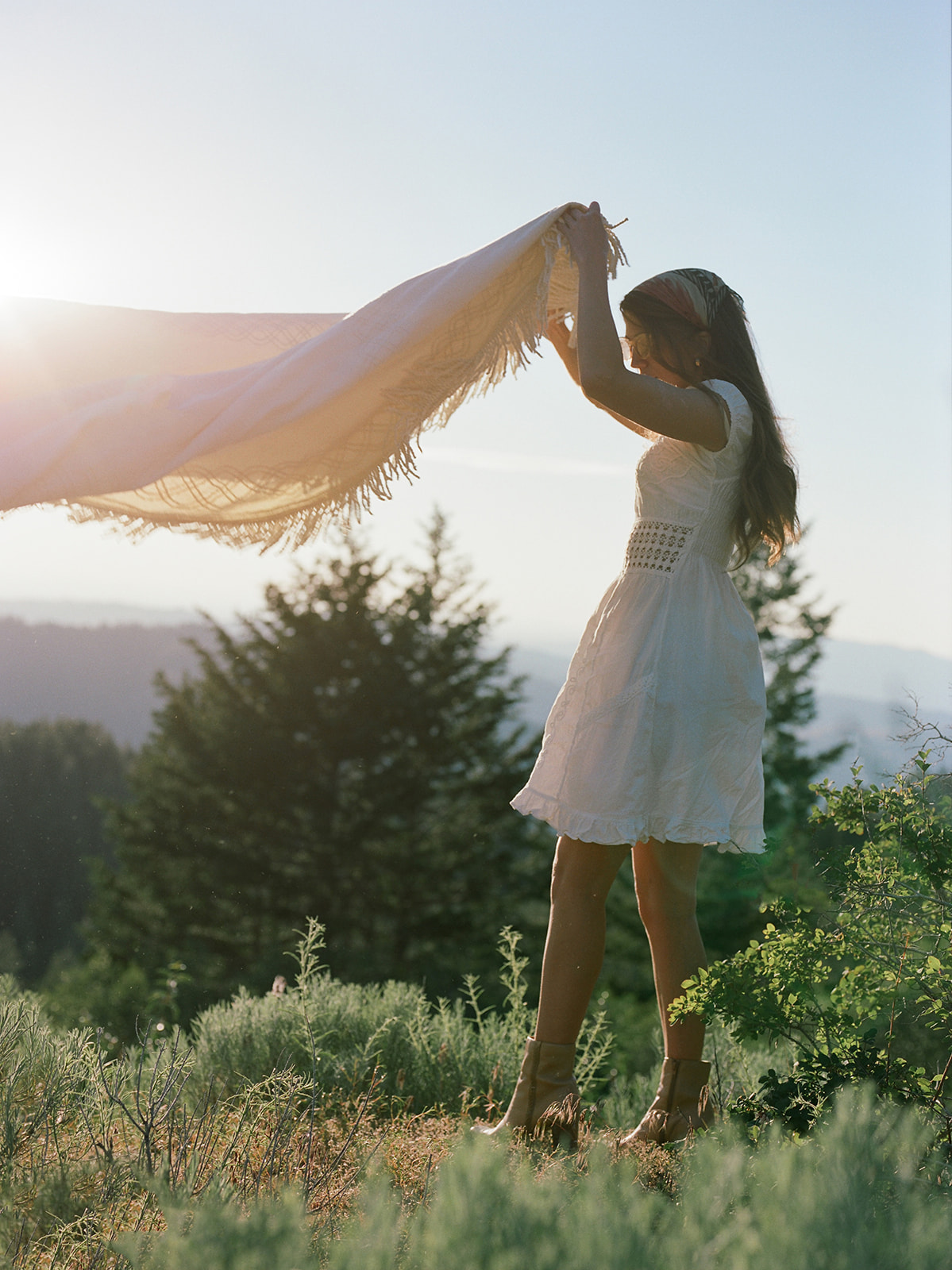 A woman setting up a picnic photoshoot. She is a wearing a white dress. The scenic area is a grass field in Utah.