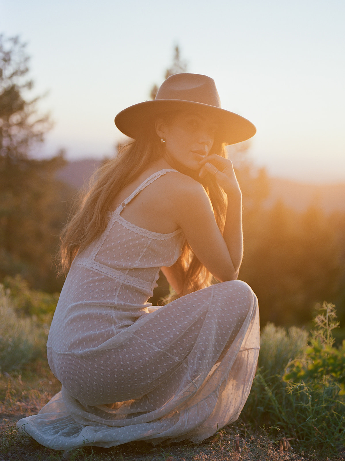 a woman posing for a summer picnic shoot in the pacific northwest. she wears a sheer ivory dress and wide brim hat