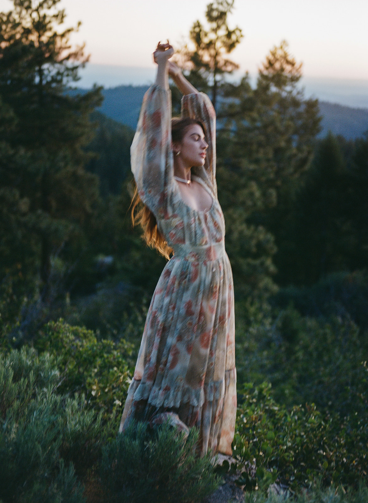 A woman posing for a picnic photoshoot. She is a wearing a maxi floral dress. The scenic area is a grass field in Utah.