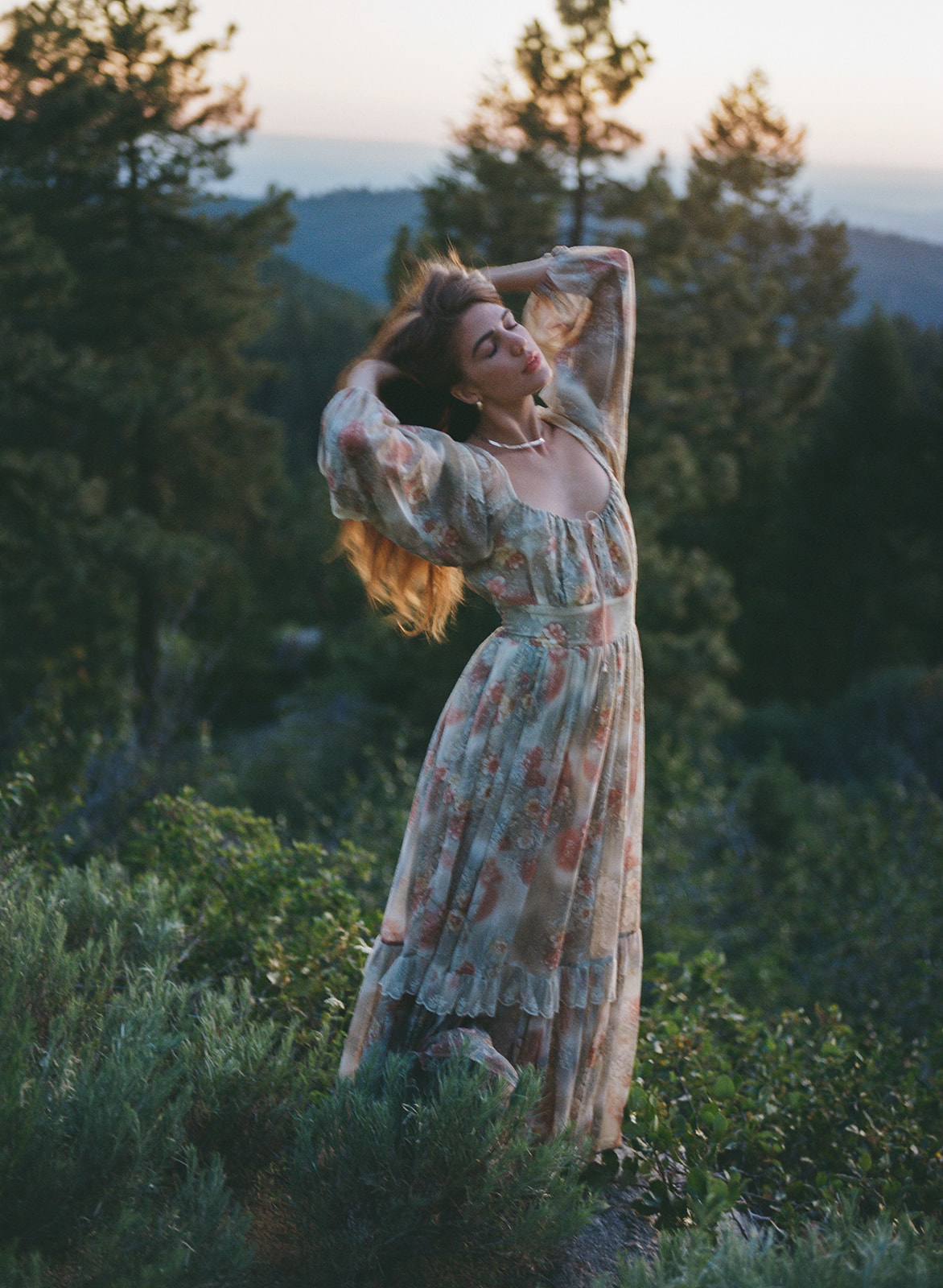 A woman posing for a picnic photoshoot. She is a wearing a maxi floral dress. The scenic area is a grass field in Utah.
