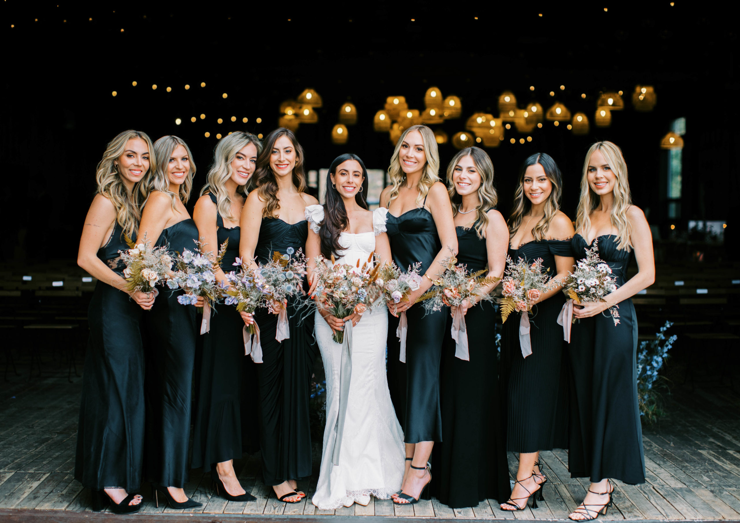 an image of a bride posing with her bridesmaids at this eclectic ranch wedding in utah at the lodge at blue sky. the bridesmaids wear mismatched black bridesmaids dresses and carry eclectic bouquets