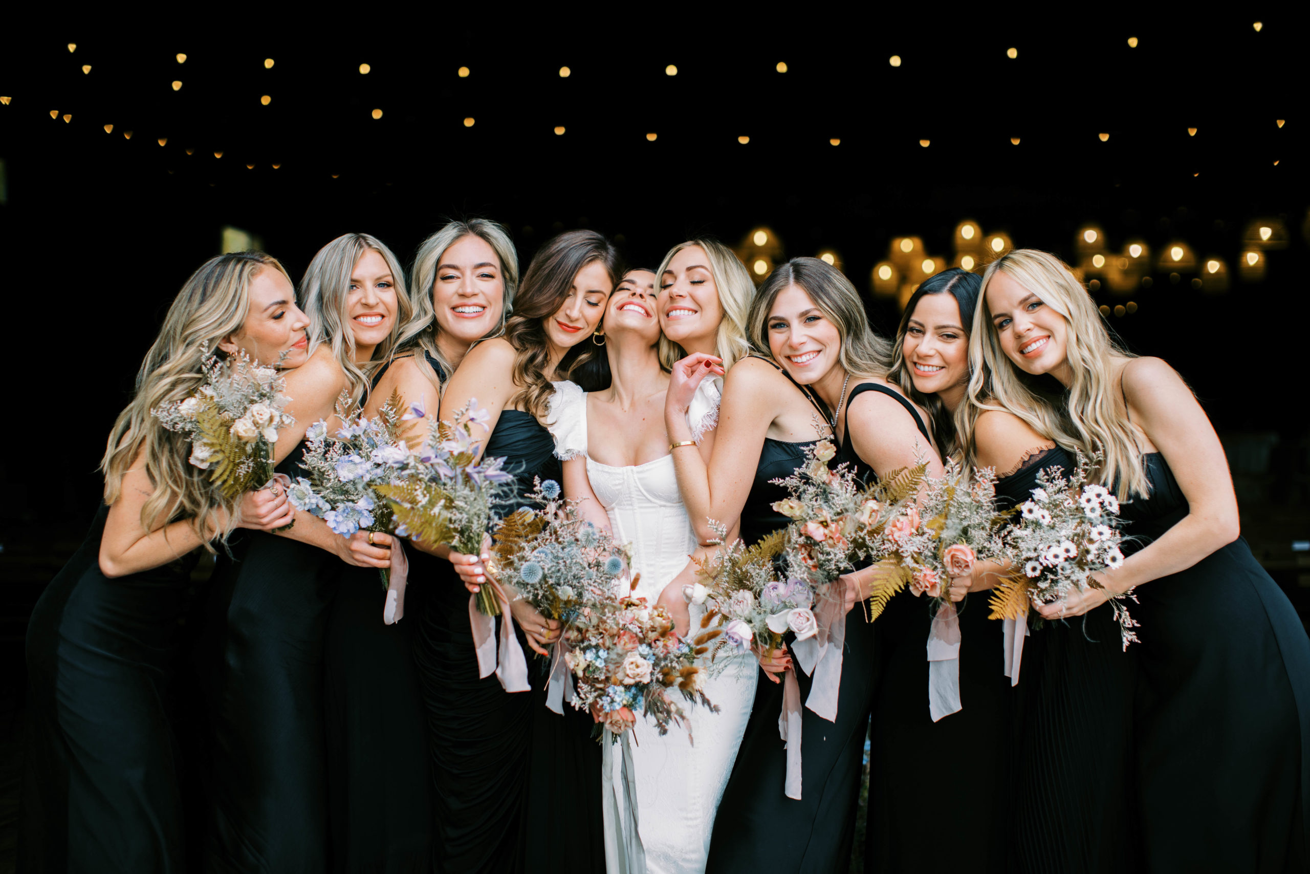group of bridesmaids hugs the bride wearing mismatched black wedding dresses for an eclectic utah ranch wedding at the lodge at blue sky. photo by megan robinson photography
