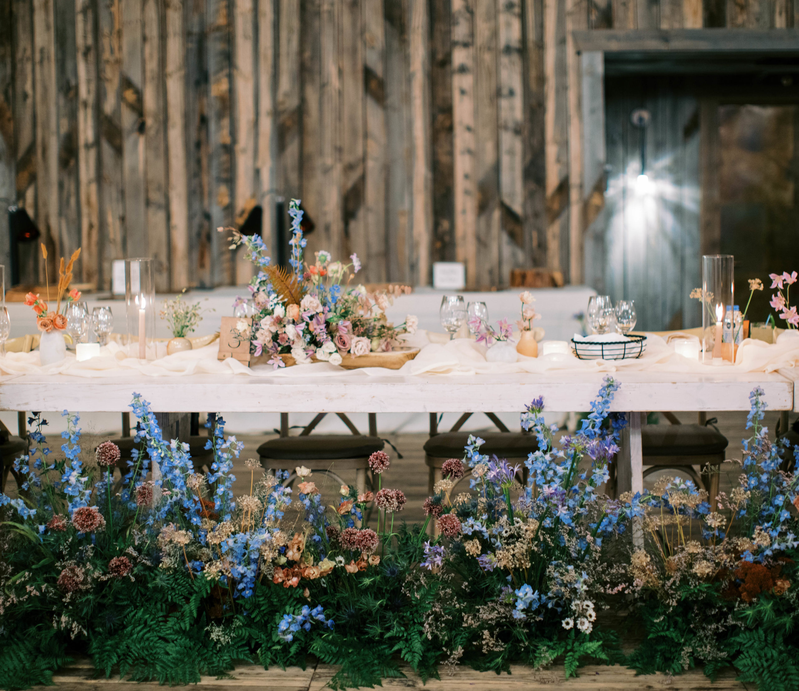 wildflower wedding reception decor, flowers line the front of the head table at this garden aesthetic wedding at blue sky ranch in utah. photo by megan robinson photography