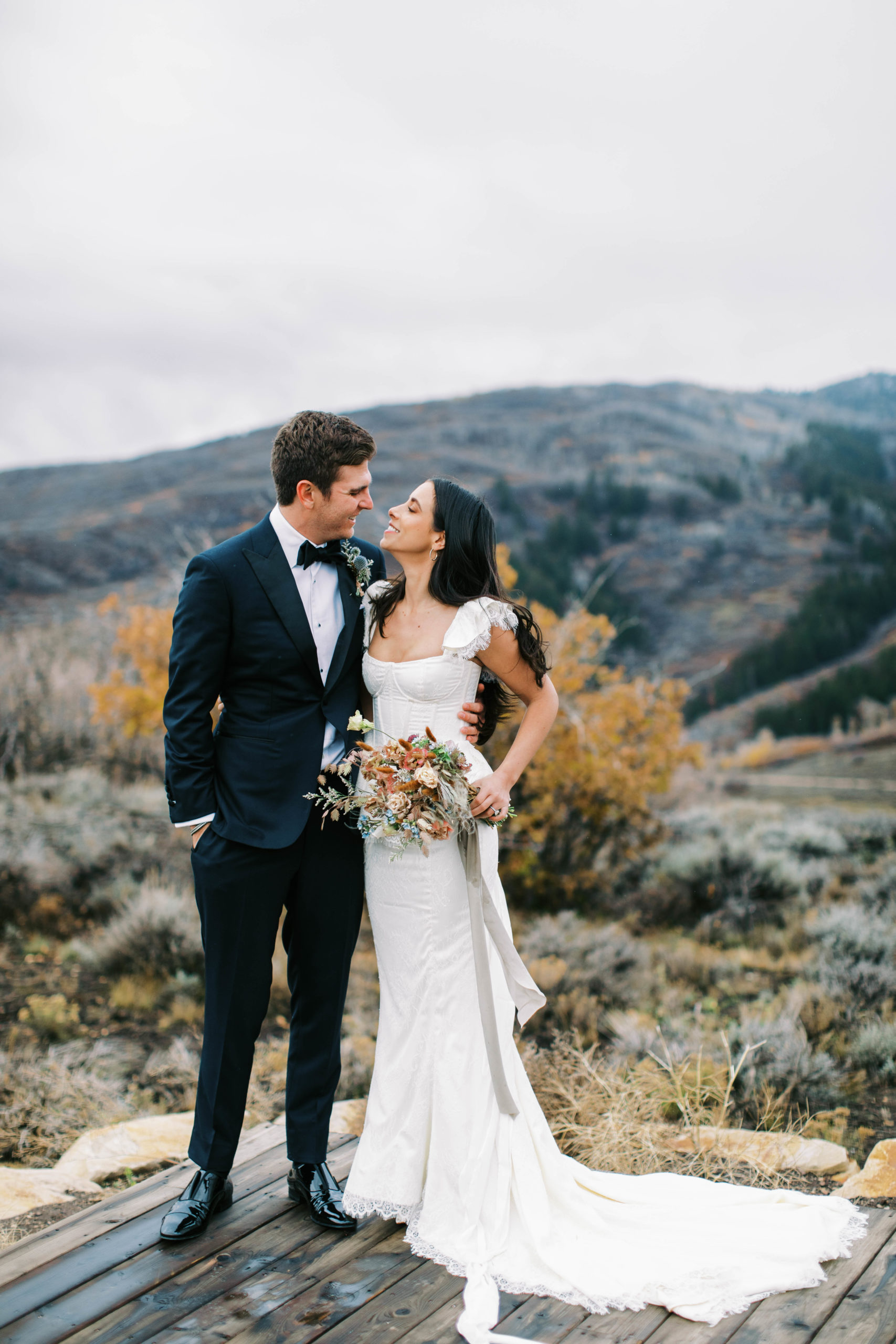 bride and groom posing together at their vintage park city ranch wedding. they smile at one another and there are mountains in the background. photo taken by megan robinson photography