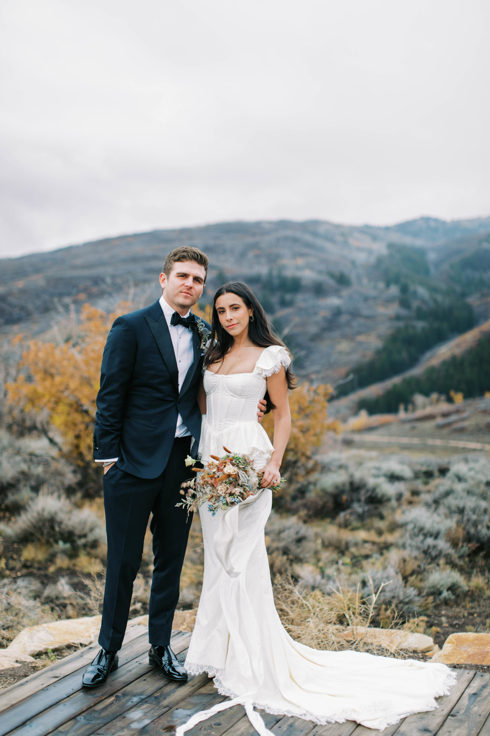 a bride and groom pose together for wedding portraits with mountains behind them at blue sky ranch in utah. photo taken by megan robinson photography