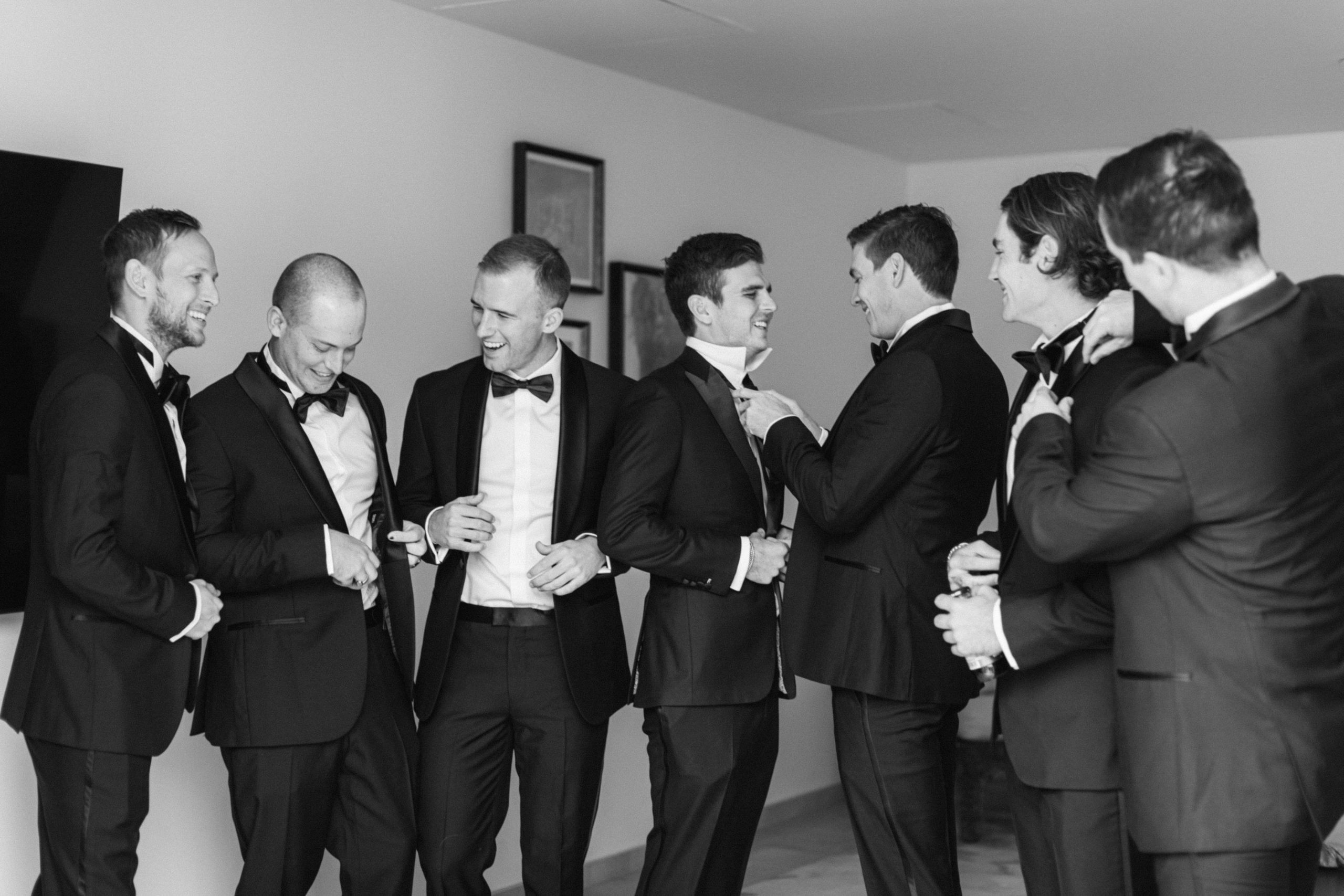 groomsmen laugh and help each other with their ties as they get ready for a utah ranch wedding