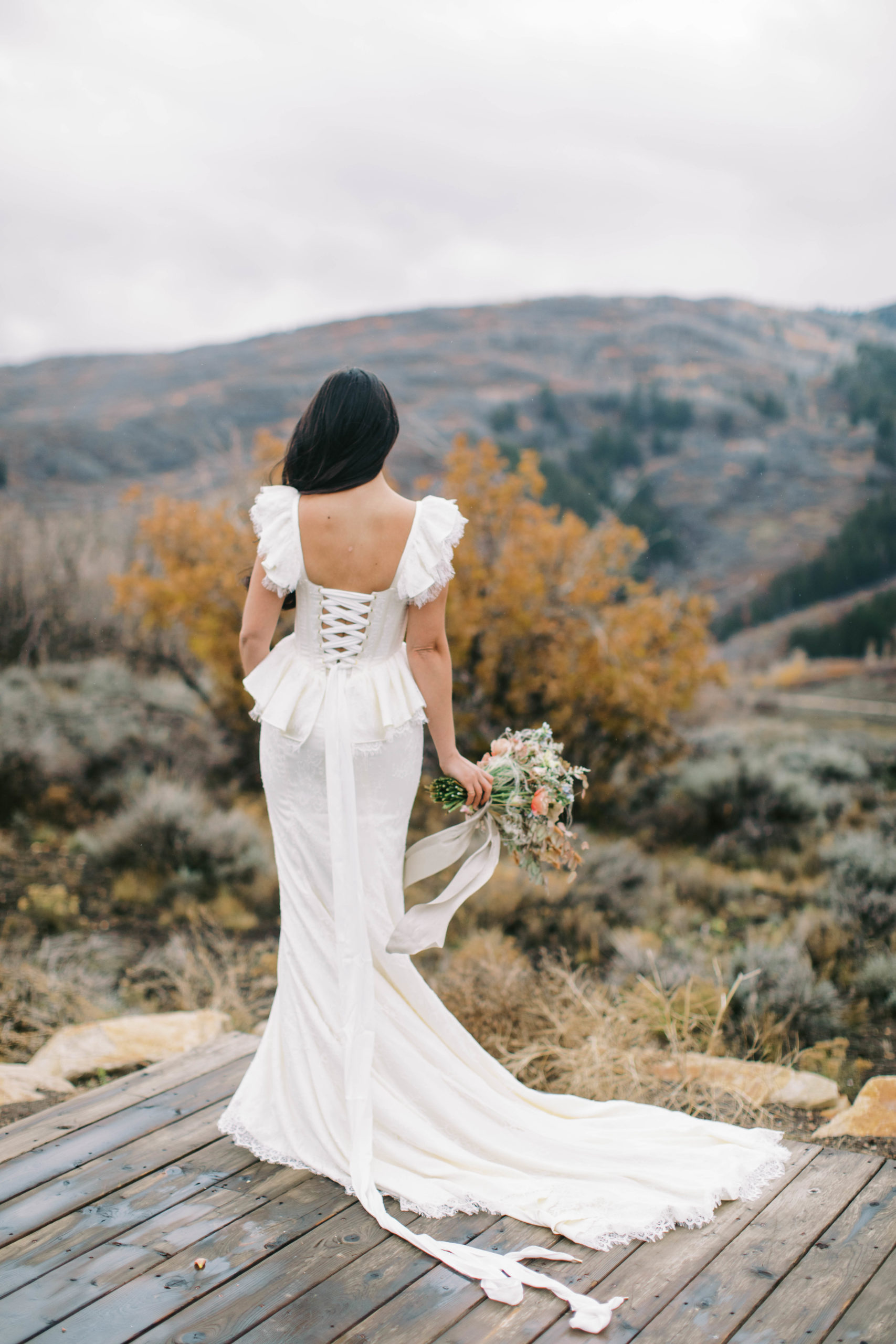 a bride wearing a vintage lace wedding dress faces away looking at the mountains at her utah ranch wedding. photo taken by megan robinson photography