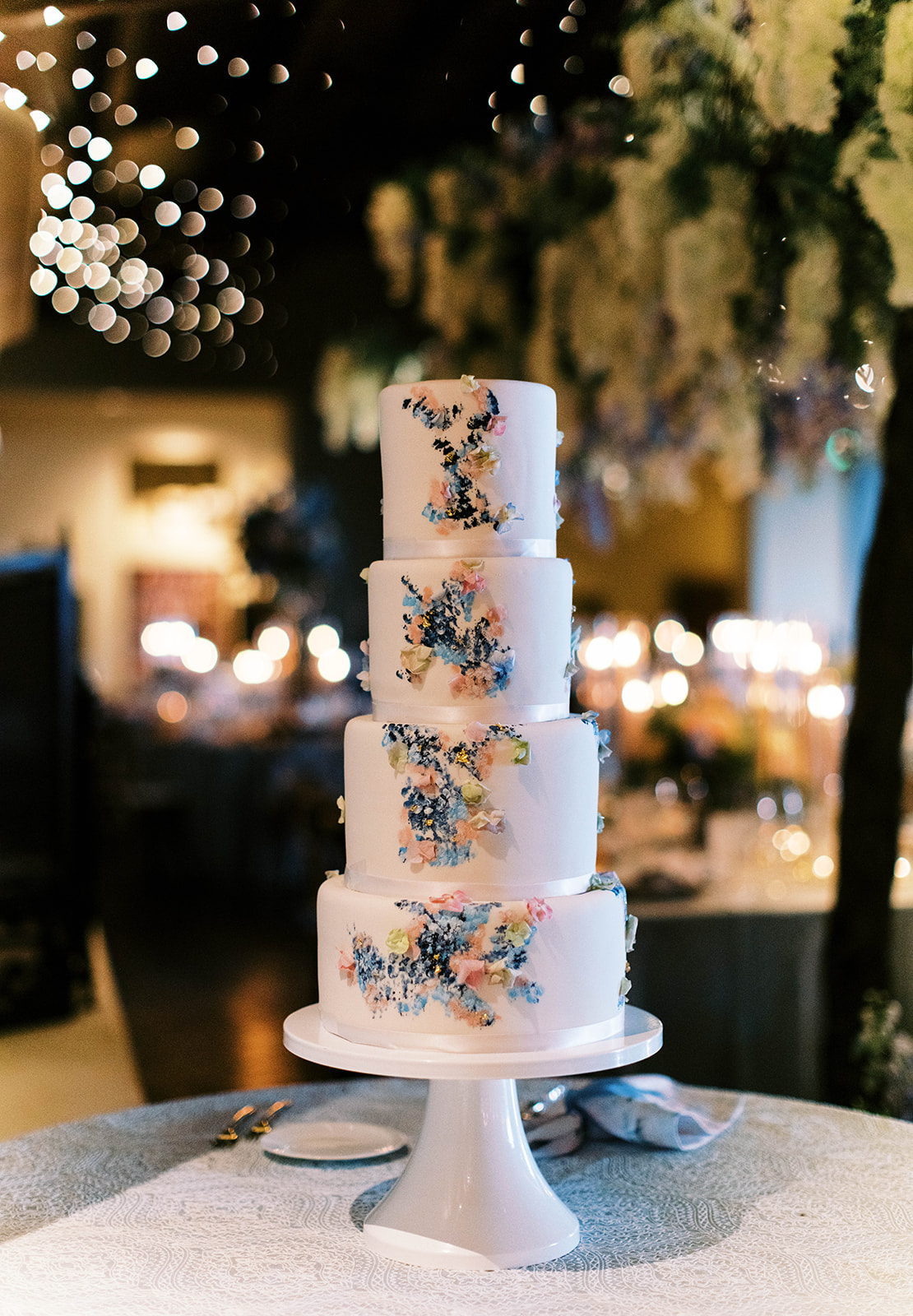 a garden party four tier white wedding cake with painted pastel flowers. photo by megan robinson photography