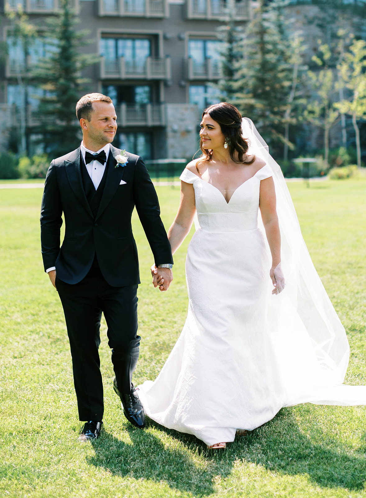 a bride and groom walk together wearing a classic groom black tuxedo and off the shoulder lace wedding dress after their ceremony at montage deer valley in park city utah. photo by megan robinson photography
