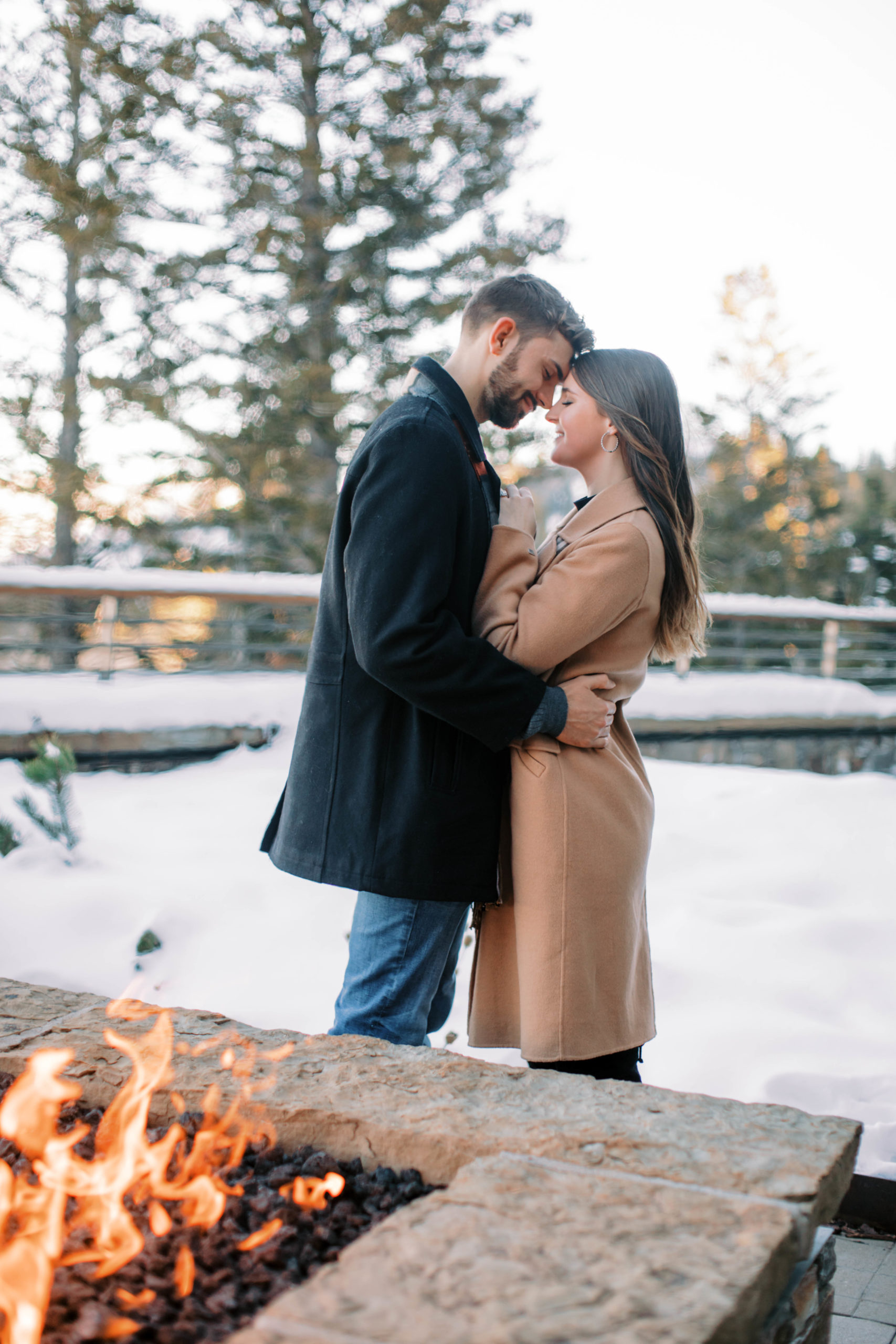 a couple hold each other in front of a fire during an outdoor winter engagement photos in park city utah. photo taken by Megan Robinson Photography