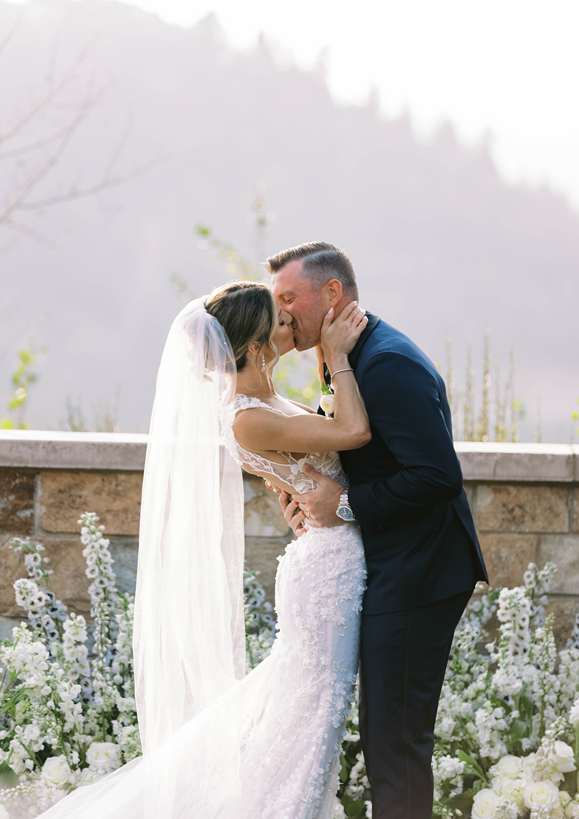 a couple kiss surrounded by white wedding flowers at their st regis deer valley wedding ceremony