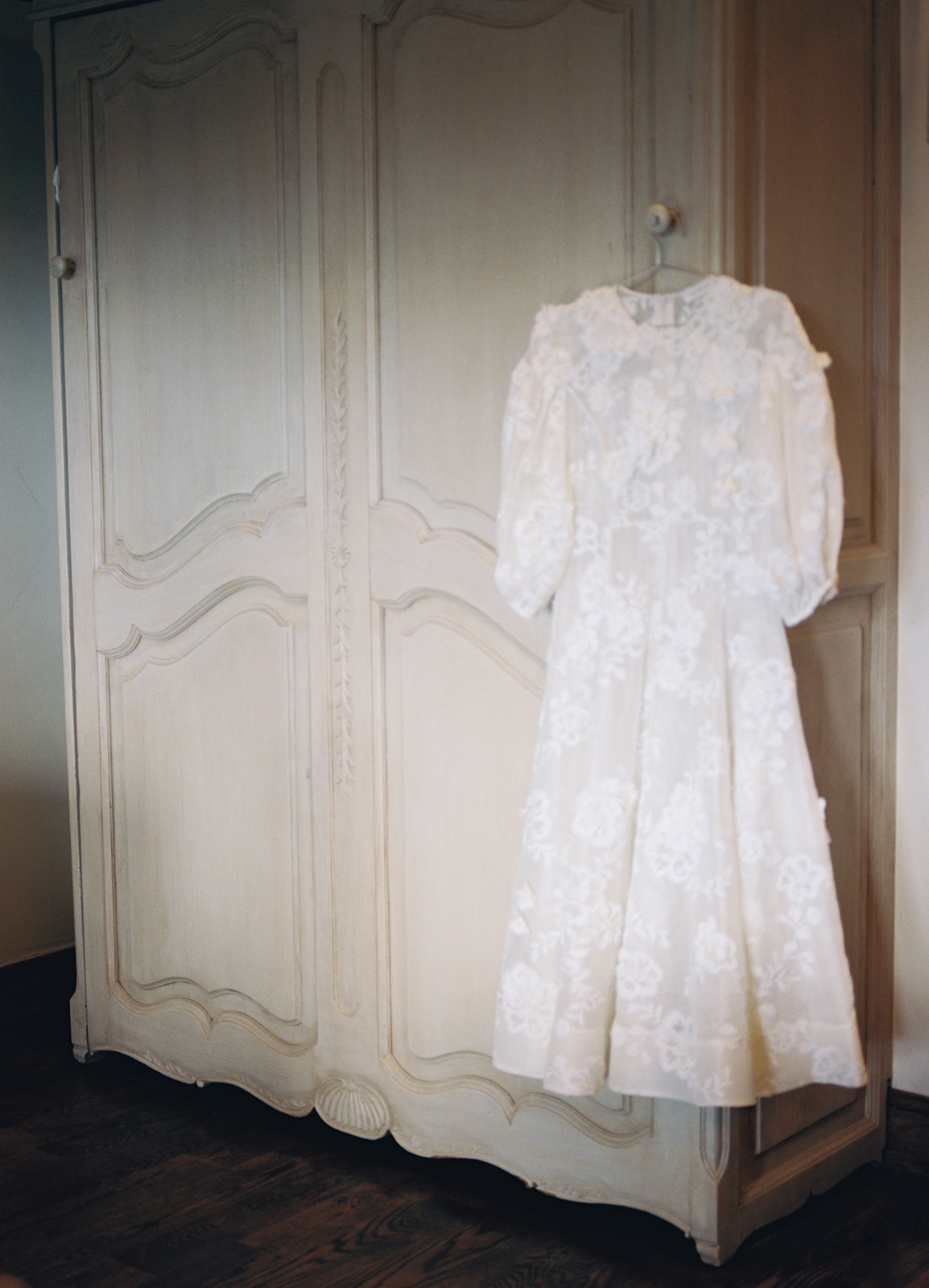 a brides tea length lace wedding dress hanging in the bridal suite