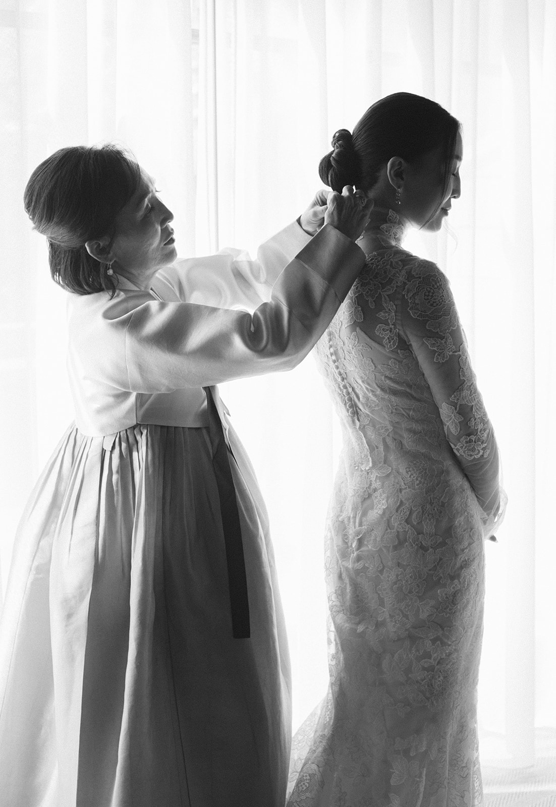 mom helps daughter get into her wedding dress black and white