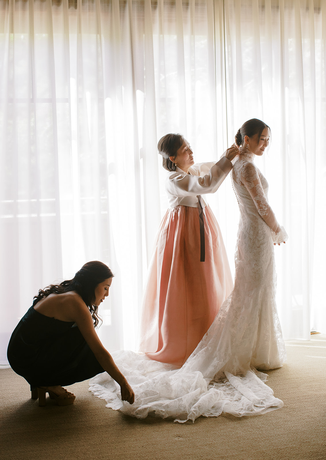 mom and bridesmaid helps young bride get into her wedding gown