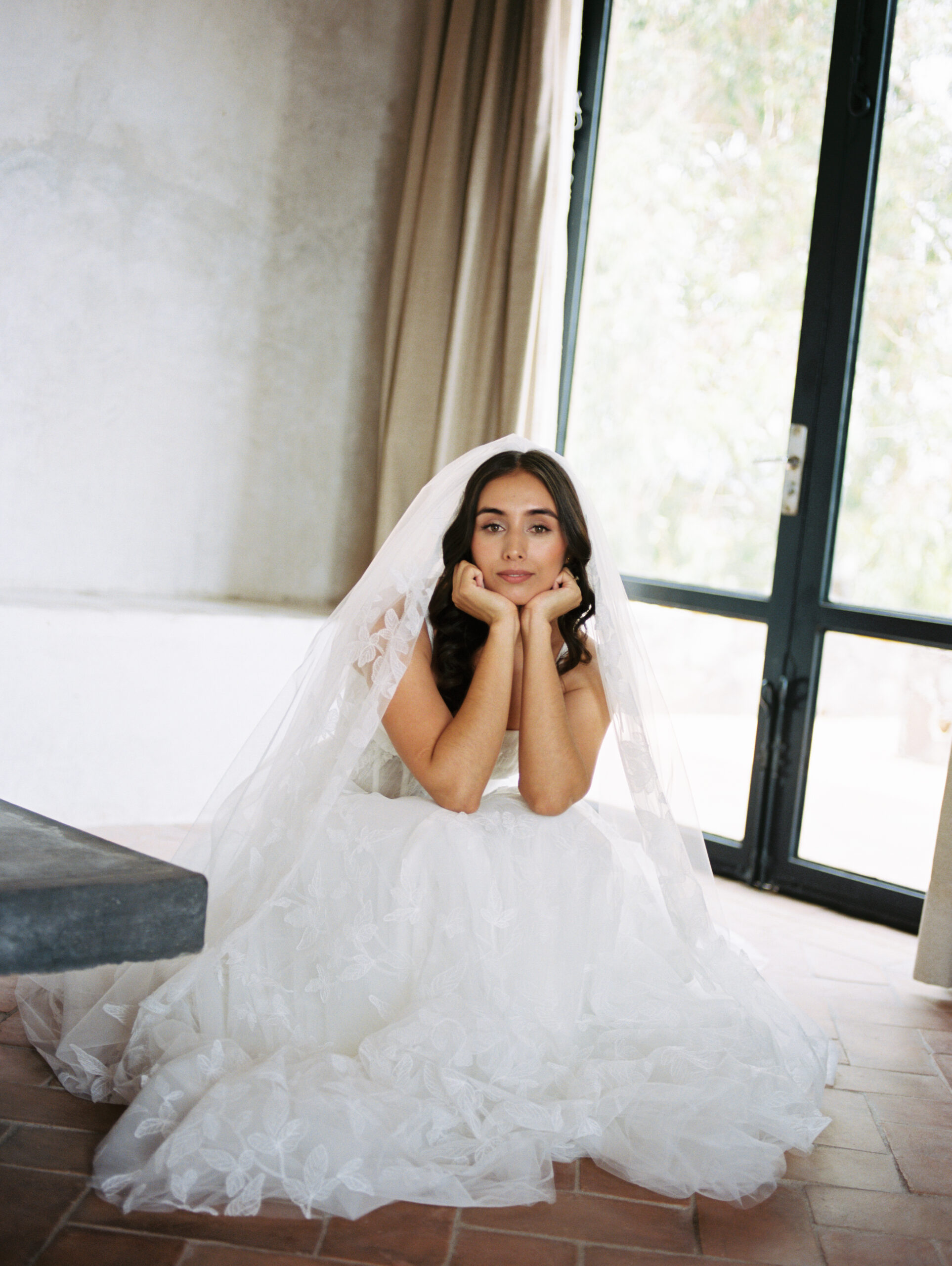 bride sitting down with her hands under her chin in a wedding dress