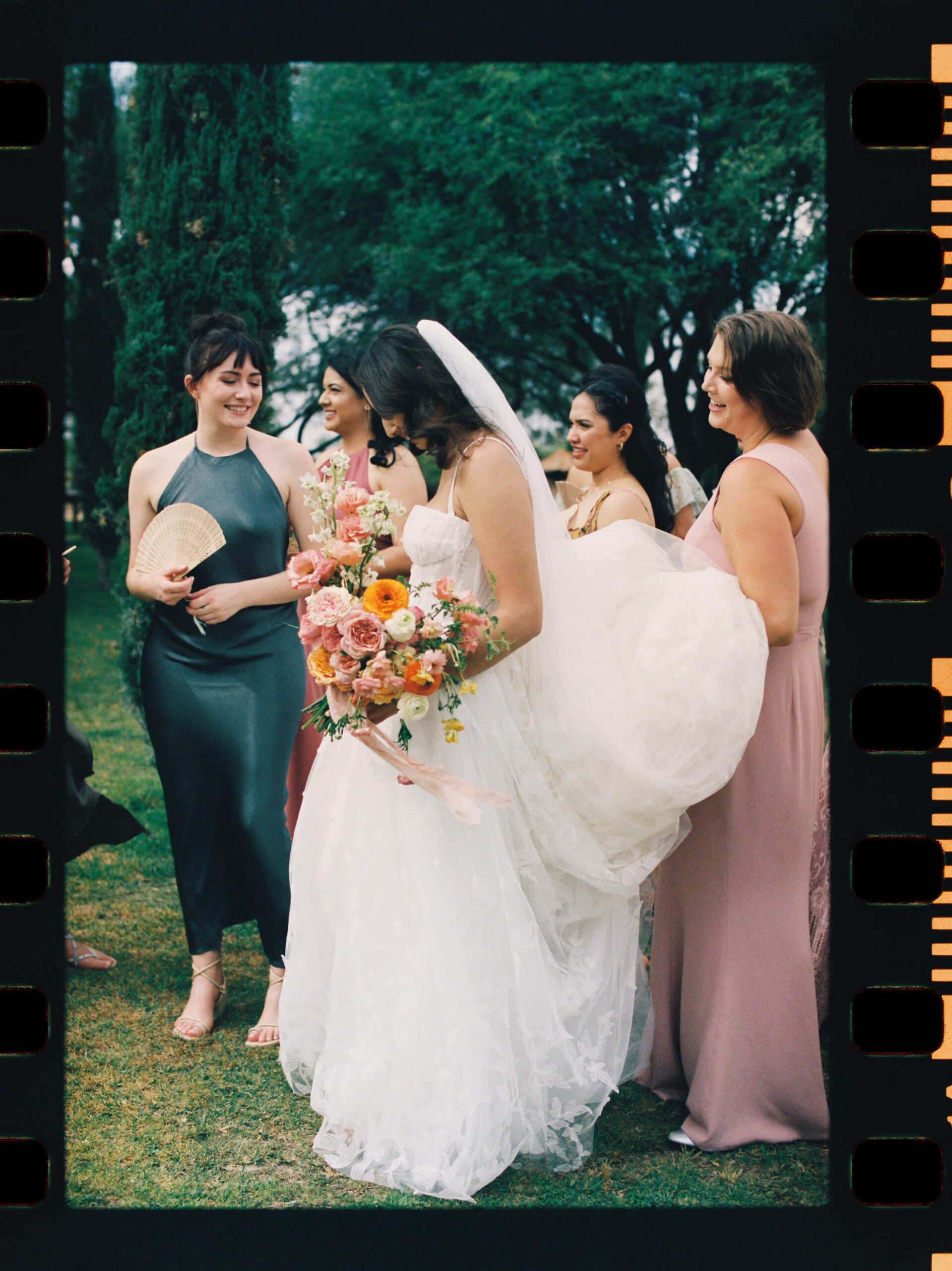 a film photo of a bride laughing with her bridesmaids, holding a bouquet 